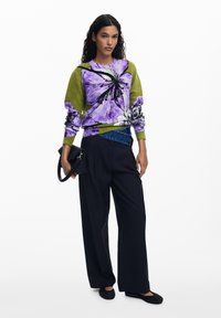 Floral patterned sweater in purple and green, paired with black wide-leg pants and a black clutch. Textured fabric and relaxed fit.