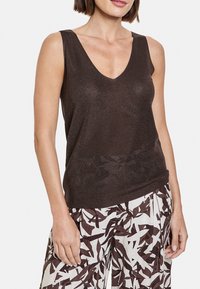 Brun ribbad linne med djup V-ringning, med en avslappnad passform. Bärs tillsammans med vita byxor som har ett brunt abstrakt bladmönster.