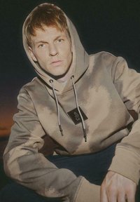 Brązowy hoodie z gradientową teksturą, z kieszenią kangurką, kapturem z sznurkiem oraz małą czarną metką z przodu.