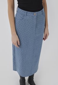 Jupe à motifs bleu clair avec un design droit, dotée de poches avant, d'une fermeture à bouton et d'une texture douce. Associée à des bottes noires montantes.