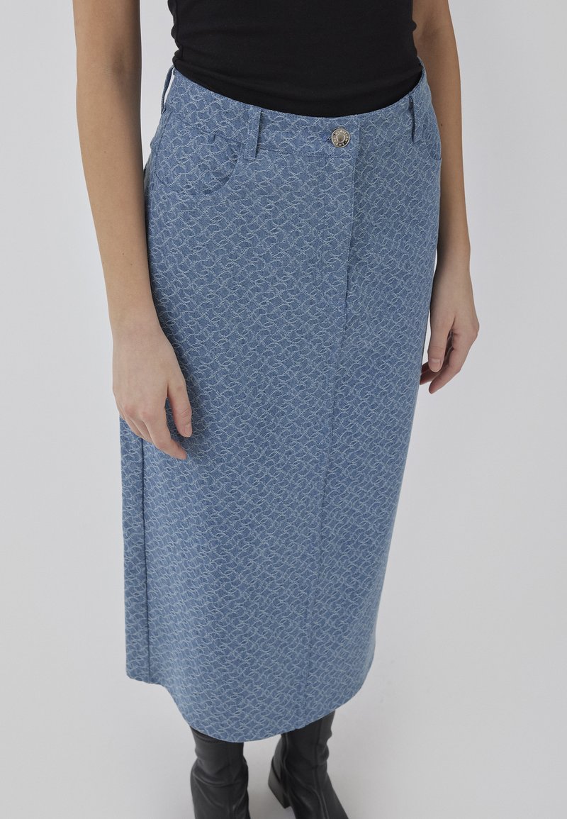 Jupe à motifs bleu clair avec un design droit, dotée de poches avant, d'une fermeture à bouton et d'une texture douce. Associée à des bottes noires montantes.