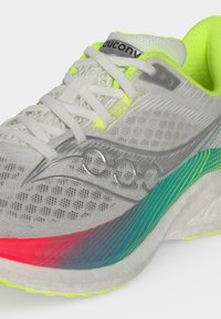 Ανοιχτό γκρι αθλητικό παπούτσι Saucony με λευκά κορδόνια, νεον κίτρινη επένδυση και πολύχρωμη σόλα με τόνους σε τιρκουάζ και κόκκινο.