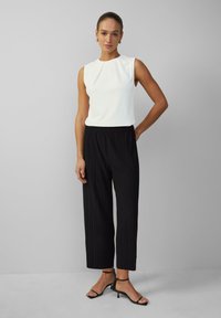 White sleeveless top with pleats paired with black, pleated, wide-leg trousers, and black strappy heeled sandals. Simple design and comfortable fit.