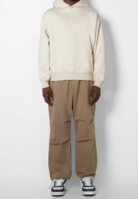 Huvtröja i ljusbeige med en strukturerad yta, kombinerad med beige byxor med elastiska muddar och svartvita sneakers.