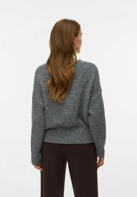 Szary sweter dziergany o luźnym fasonie, z opuszczonymi ramionami i ściągaczem u dołu. Tekstura jest miękka, a wzór cechuje się prostą, klasyczną sylwetką.