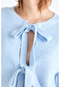 Cardigan tricoté bleu clair avec un col rond, avec deux liens en tissu à l'avant et une texture côtelée.