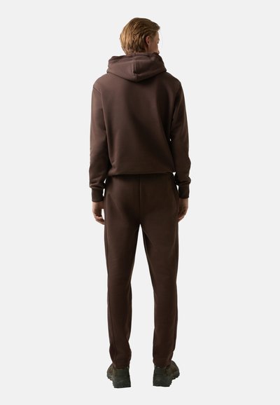 Brun bomulds hoodie med en stor hætte, ribbede manchetter og matchende træningsbukser. Outfitten har en glat tekstur og en løs pasform.