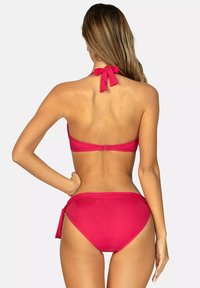 Czerwony bikini ze żłobionym wykończeniem, z górą w stylu halter na wiązanie z tyłu oraz wysokim stanem majtek z bocznymi troczkami.