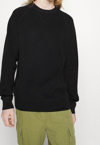 Zwarte crewneck sweatshirt van textuurstof, met ribgebreide manchetten en zoom, en raglanmouwen, gecombineerd met groene cargobroek.