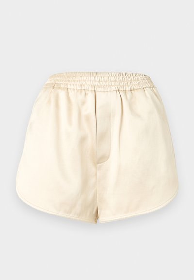 Σορτς με ελαστική μέση σε ανοιχτό μπεζ χρώμα, με απαλό ύφασμα και καμπύλες ραφές, απλωμένα επίπεδα σε ανοιχτό γκρι φόντο.