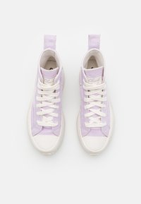 Tenisky vysoké typu hi-top ve světlém levandulovém plátně s bílými gumovými podrážkami a šňůrkami. Mají logo na jazyku a poutka na patě.