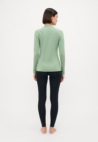 Langermet, lysegrønn rashguard med en glatt tekstur, kombinert med tettsittende svarte leggings. Ingen synlige mønstre eller detaljer på antrekket.