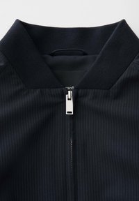 Collar and zipper of a dark navy jacket with subtle vertical pinstripes, featuring a silver rectangular zipper pull.