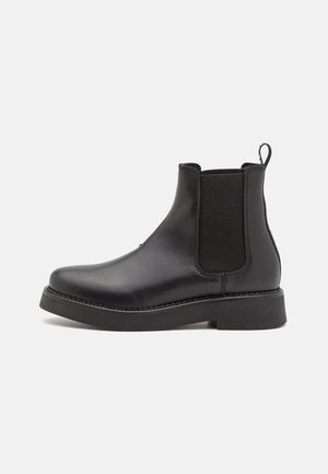 Black Chelsea boots, made of smooth leather, feature elastic side panels, round toe, chunky sole, and a pull tab at the back.