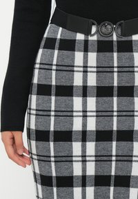 Fustă în carouri alb-negru cu design conic, fabrică texturată și curea neagră cu o cataramă rotundă decorativă.