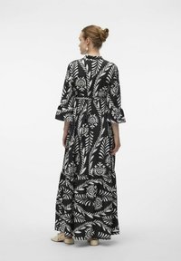 Robe maxi avec un motif floral noir et blanc, dotée de manches évasées, d'une taille marquée et d'un design de jupe à volants.