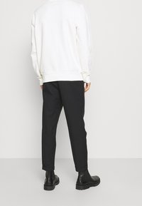 Felpa bianca in cotone con polsini a coste, abbinata a pantaloni neri a gamba affusolata e stivali alla caviglia in pelle nera. Design semplice, dettagli minimali.