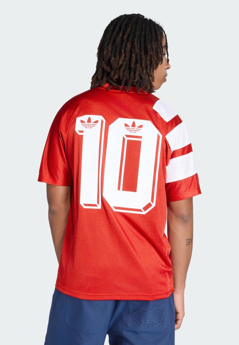 Personne avec des dreadlocks porte un maillot de sport rouge avec des rayures blanches sur les manches et un grand numéro 10 blanc dans le dos.