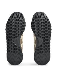Black rubber shoe soles with a wavy tread pattern, featuring beige upper sections and a distinctive accent detail near the heel.