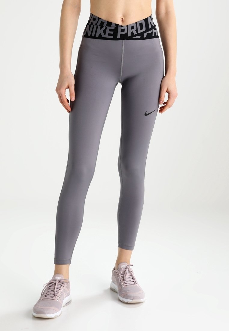Nike Pro leggings i grå med en høj sort talje med logo, glat tekstur og tætsiddende design. Båret med lyserøde sneakers.