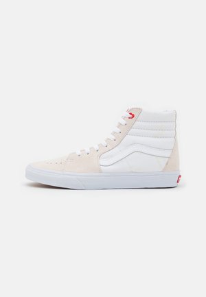 High-top sneaker med hvidt læder og beige ruskindspaneler, hvide snørebånd, hvid stribedetalje og rød snørehulsaccent.