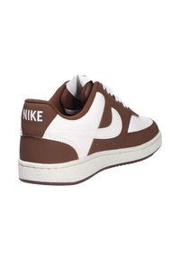 Zapatillas Nike con una parte superior de cuero blanco y acentos marrones, un collar acolchado y una suela de goma texturizada. Marca mostrada en el talón.