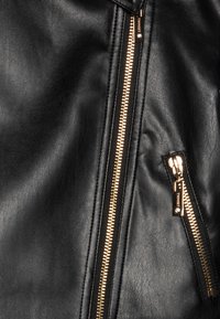 Black leather jacket featuring gold zippers. Visible side zipper and pocket detail. Smooth texture with a matte finish.