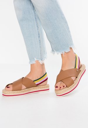 Sandales en cuir marron avec un design croisé, semelle de style espadrille et bande élastique rayée multicolore. Bout ouvert, hauteur de plateforme visible.