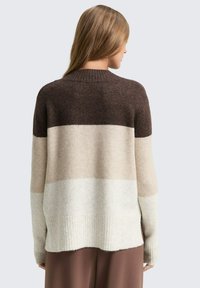 Maglione oversize nelle tonalità di marrone, beige e crema. Tessuto lavorato a maglia morbido con colletto e orlo a coste, caratterizzato da un design a blocchi di colore.