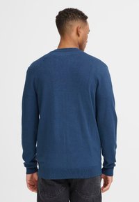 Maglione blu lavorato a maglia con maniche lunghe, polsini e orlo a costine, presenta un classico scollo rotondo e una consistenza liscia e morbida. Design semplice.