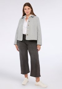 Jachetă gri, texturată, cu guler și patru butoane mari, asortată cu blugi negri, evazați și adidași albi.