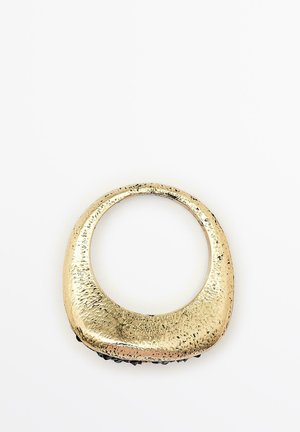 Accessorio in metallo lucido color oro con forma ovale curvata; superficie testurizzata con sottili variazioni e un bordo inferiore nero liscio.