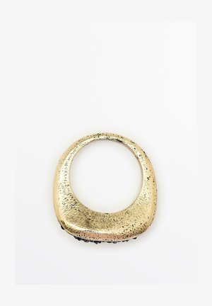 Accessorio in metallo lucido color oro con forma ovale curvata; superficie testurizzata con sottili variazioni e un bordo inferiore nero liscio.