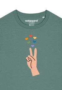 Groene t-shirt met een grafisch ontwerp van een hand die een vredesteken maakt, omringd door kleurrijke hartvormen in verschillende kleuren en maten.