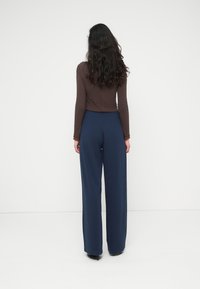 Καφέ μα κρυμάνικο τοπ και σκούρο μπλε παντελόνι με φαρδιά μπατζάκια. Το σύνολο διαθέτει εφαρμοστό τοπ με cropped σιλουέτα και λείο ύφασμα.