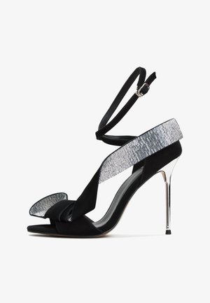 Crne suede sandale s visokim potpeticama s širokom trakom ukrašenom rhinestones-ima, čvorastim detaljem sprijeda i remenom oko gležnja s kopčom.