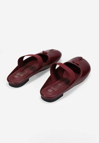Zapatos de cuero burdeos tipo slip-on con punta redondeada, correas elásticas y plantilla texturizada. Suela de goma negra baja y detalle decorativo de nudo.