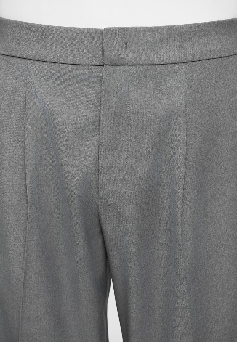 Pantalons ajustés gris avec une texture lisse, présentant un devant plat, des coutures soignées et une coupe slim.
