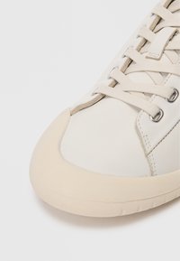 Λευκό δερμάτινο sneaker με στρογγυλή καπάκι από καουτσούκ, επίπεδες κορδόνια και μεταλλικά μάτια. Υφή στο πλαινό πάνελ με λεία επιφάνεια στο επάνω μέρος.