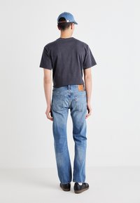 Camiseta de algodón gris oscuro, jeans de mezclilla azul claro y una gorra azul. Los jeans tienen un parche de cuero, bolsillos traseros y un diseño de pierna recta.