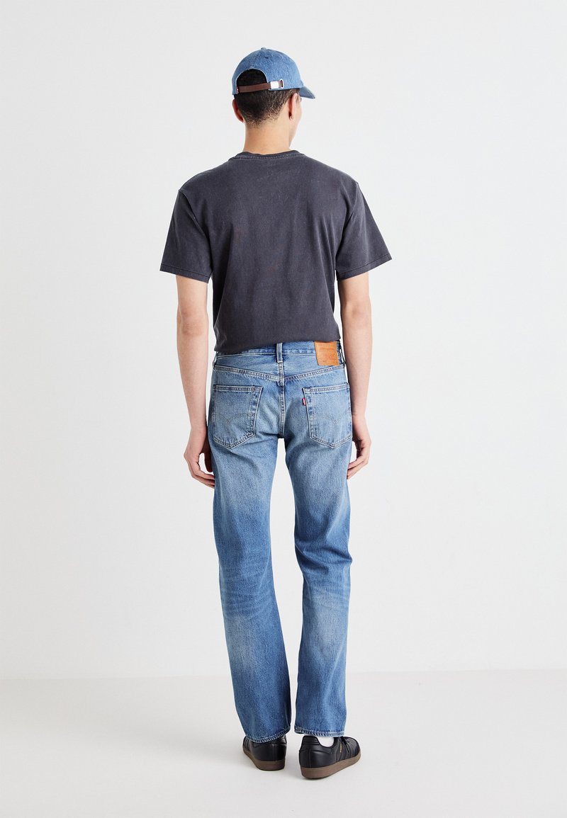 Dunkelgraues Baumwoll-T-Shirt, hellblaue Jeans und eine blaue Kappe. Die Jeans verfügen über einen Lederpatch, Gesäßtaschen und einen geraden Schnitt.