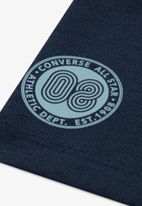 Ναυτικό ύφασμα με κυκλικό μπλε λογότυπο που απεικονίζει το «Converse All Star», «Athletic Dept.» και «Est. 1908». Υφή φόντου με διακριτικές ραφές.