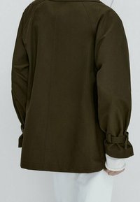Veste vert khaki avec une coupe décontractée, dotée de manches resserrées et d'un empiècement au dos. Le tissu est lisse avec une finition mate.