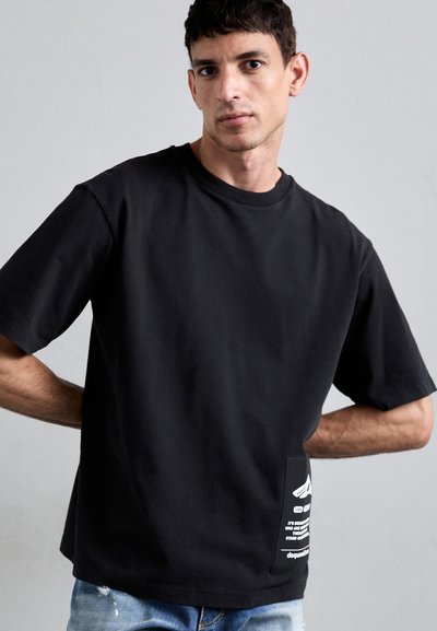 Black short-sleeve t-shirt made of cotton, featuring a front pocket with white text and design elements, paired with light blue distressed jeans.