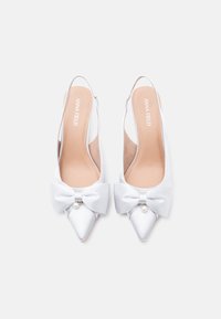 Άσπρα ψηλοτάκουνα πέδιλα από σατέν με λουρί, μυτερή μύτη, μεγάλο φιόγκο και διακοσμητικό μαργαριτάρι. Τα εσωτερικά πέλματα είναι μπεζ με λευκή επωνυμία.