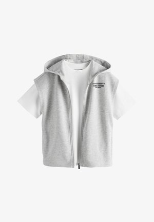 Biele tričko s krátkym rukávom a okrúhlym výstrihom, vrstvené so svetlošedou bezrukávovou mikinou na zips s kapucňou a malým čiernym textom na hrudi.