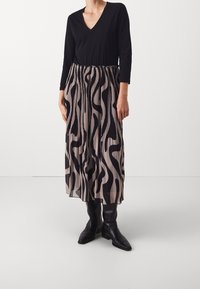 Plisserad kjol med ett svart abstrakt mönster på en beige bakgrund, i kombination med en svart långärmad topp och svarta knähöga stövlar.