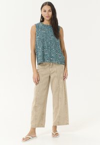 Haut sans manches à motifs turquoise associé à un pantalon large beige. La tenue présente une coupe décontractée et des détails de couture subtils.