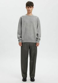 Grå strikket genser med rund hals, oversized passform og ribbestrikkede mansjetter, kombinert med løstsittende mørkegrønne rutete bukser og svarte sko.