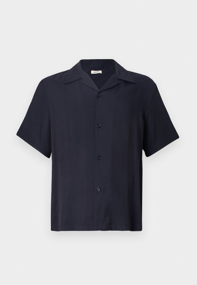 Trumpas rankovėmis, mygtukais užsegamas marškinis tamsiai mėlynos spalvos, pagamintas iš glotnaus audinio. Turi apykaklę, penkis mygtukus priekyje ir laisvą siluetą.